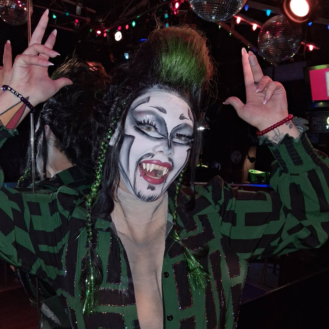 Dyke Tyson in monster drag with signature mohawk, fangs, and green-and-black costume during a live performance